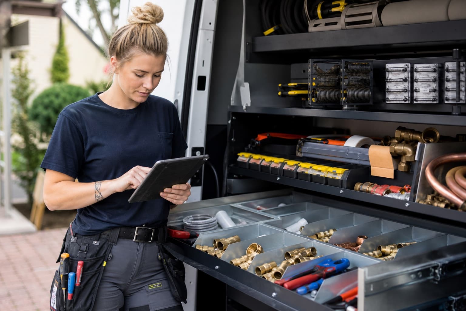 A young plumber reviewing her work beside an organized service van